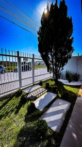a white fence with a tree next to a sidewalk at Hotel Pousada Litorânea in Tijucas