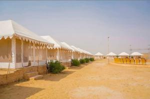 Una hilera de tiendas blancas en un campo desértico en Sam Dunes desert Safari Camp, en Jaisalmer