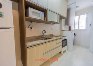 une cuisine avec un évier et un micro-ondes dans l'établissement Apartamento na Praia Grande a 500m Praia do Forte, à Praia Grande