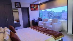 a bedroom with a bed and chairs and a large window at Palette Hotel and Resort Kankarbagh Main Road Formerly Aalcajars Inn in Bankipur