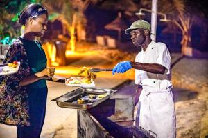 una donna sta servendo un piatto di cibo a un uomo di Balafon Beach Resort a Kololi