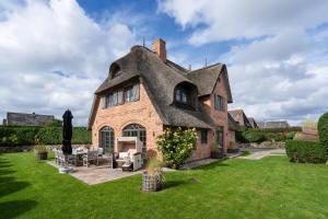 a house with a thatched roof on a lawn at Villa Hengist mit eigener Sauna, 600 Meter vom Weststrand, Wenningstedt, Sylt in Wenningstedt