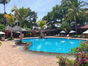 a large blue swimming pool with palm trees and umbrellas at Apartemen 6236 at Jayakarta Residence Bali in Seminyak
