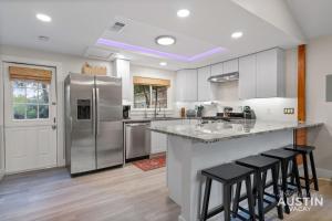 a kitchen with a refrigerator and some bar stools at Pet Friendly 3BR 3BA Hill Country Home w Private Pool and Grill by Austin Vacay in Buffalo Gap