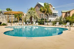 a swimming pool with chairs and umbrellas in front of a house at Poolside Fun & Ocean Strolls: Harbor Island Haven! in Fripp Island