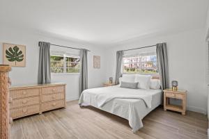 a white bedroom with a bed and two windows at Steps To Beach! 4 Condos In 1- Perfect For Groups in West Palm Beach