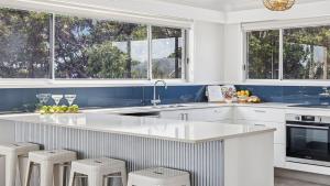 a kitchen with white cabinets and a counter with stools at Pandanus - Spacious Waterfront Escape with Private Pontoon & Pool - Holiday Yamba in Yamba