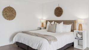 a white bedroom with a large bed with white pillows at Pandanus - Spacious Waterfront Escape with Private Pontoon & Pool - Holiday Yamba in Yamba +12 photos