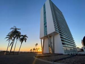a building on the beach with palm trees and the sunset at Beachfront Apartment in Mazatlán