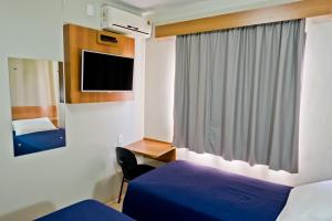 a bedroom with two beds and a desk and a tv at Tri Hotel Centro Chapecó in Chapecó