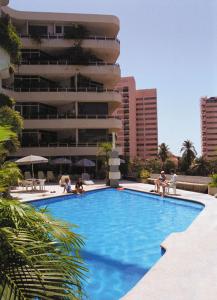 a swimming pool with people sitting on chairs in front of a building at Hotel Suites Jazmín Acapulco in Acapulco