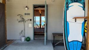 Una puerta de una casa con una tabla de surf al lado. en 奄美ゲストハウス sou 海と森のテラス 2025年夏オープン, en Tatsugo