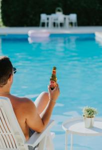 a man sitting in a chair holding a bottle of beer by a pool at Jerónimos Garden & Pool Villas in Lamego