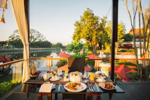 a table with food on a balcony with a view of a river at RatiLanna Riverside Spa Resort in Chiang Mai