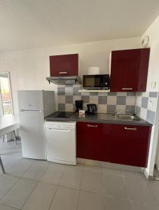 eine Küche mit weißen Geräten und roten Schränken in der Unterkunft T3 & tous conforts & piscine & sauna & plage in Argelès-sur-Mer