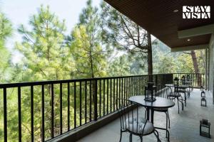a balcony with tables and chairs and a view of trees at StayVista at Uno - The Himalayan Den with Jacuzzi in Barog