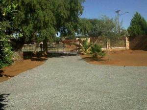 a gravel driveway with a fence and a tree at Chrisand Guesthouse in Kuruman +4 photos