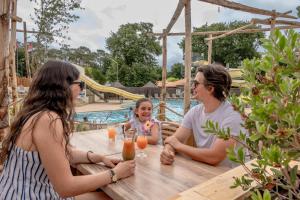 a group of people sitting around a table by a pool at Flower Camping Au Bois des Biches in Saint-Hilaire-de-Riez