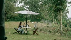 una mujer sentada en una mesa bajo una sombrilla en Thrill Playgrounds & Tipi Cafe, en Libona 7 fotos más
