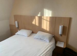 トゥールコワンにあるHôtel Le Verdyのベッド1台(白い枕2つ、木製ヘッドボード付)