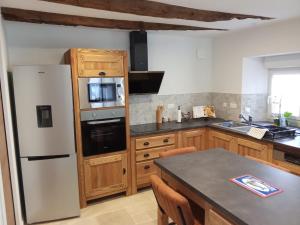 a kitchen with a white refrigerator and wooden cabinets at Petite maison de campagne avec poêle à bois, 20 mn des plages in Bréhand