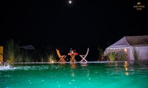 a table and chairs next to a swimming pool at night at Ranthambhore Bagh Dwar Camp in Khilchipur