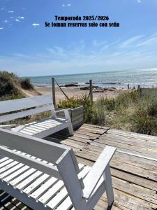 un banco blanco sentado en la parte superior de un paseo marítimo de madera en la playa en Las Piedritas Casa de Mar Loft, en Las Grutas