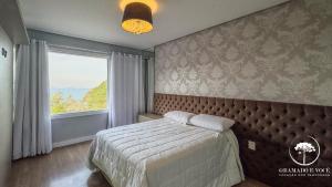 ein Schlafzimmer mit einem Bett und einem großen Fenster in der Unterkunft Casa com piscina 3 suítes a 15 min Centro Gramado in Gramado + 17 Fotos