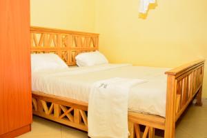 a bedroom with a wooden bed with white sheets at Baaz hotel Kakamega in Kakamega