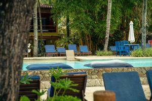 a swimming pool with blue chairs and a table and umbrella at Via Das Pedras Pousada in Morro de São Paulo