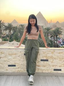 Una mujer parada en un muro con las pirámides. en New fort Night Pyramids Hotel, en Giza