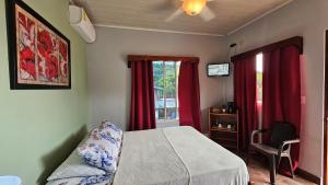 1 dormitorio con 1 cama con cortinas rojas y silla en Boquete Town Hostal, en Boquete