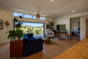 a living room with a blue couch and a large window at Te Makiri House, Onetangi - Be My Guest Waiheke in Waiheke Island