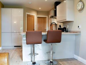 a kitchen with white cabinets and two bar stools at Stone Cottage in Wingerworth +13 photos