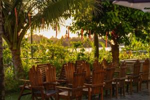 une rangée de chaises en bois assises sous un arbre dans l'établissement CocoPalm Hoi An River Beach by JM Villas, à Hội An