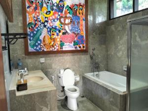 a bathroom with a toilet and a painting on the wall at Villa Biyu siyu in Ubud +2 photos
