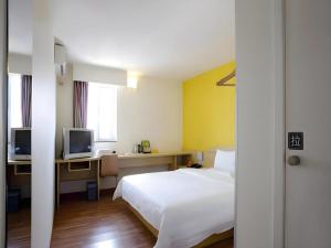 a bedroom with a bed and a desk with a television at 7 Days Inn Jixian County Baowei Road in Shuangyashan