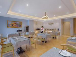 a woman standing in a restaurant with tables and chairs at Vienna Hotel Jinjiang Bus Passenger Station in Jingjiang