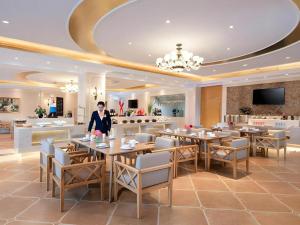 a woman standing in a restaurant with tables and chairs at Vienna Hotel Shanxi Datong High-Speed Railway Station Wanda Plaza in Datong