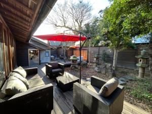 um pátio com sofás e um guarda-chuva vermelho em 古民家宿 禅楽 em Shimminato