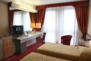 a hotel room with two beds and a desk with a television at Hotel Maxim in Verona