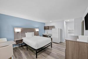 a bedroom with a white bed and a kitchen at Suburban Studios Newport News - Hampton in Newport News