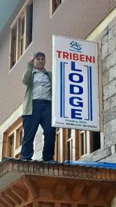 PhakdingにあるTribeni Lodge Phakdingの看板を持って建物の上に立っている男性