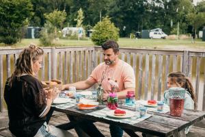 a man and two women sitting at a picnic table at Glamping bij Vakantiepark De Sallandshoeve in Nieuw-Heeten