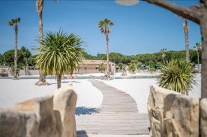 een houten promenade in het zand met palmbomen bij Mobilhome au Camping La Yole in Vendres-Plage