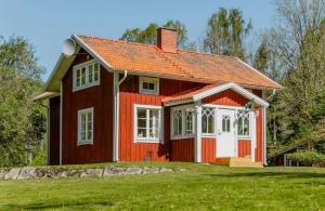 a red house with an orange roof on a green field at Relaxing Villa With Fireplace And Private Stream in Lerdala