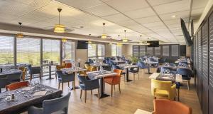 una sala da pranzo con tavoli, sedie e finestre di Best Western Côte des Sables Plouescat a Plouescat