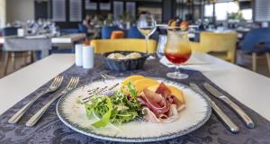 une assiette de nourriture sur une table avec un verre de vin dans l'établissement Best Western Côte des Sables Plouescat, à Plouescat