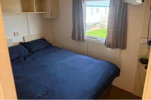 a small bedroom with a blue bed and a window at 2 Bedroom Chalet Sleeps 6 -Free Parking -Tv -WiFi in Chapel Saint Leonards