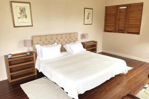 a bedroom with a large bed with white sheets and wooden floors at Pear Tree House Barbados in Saint James